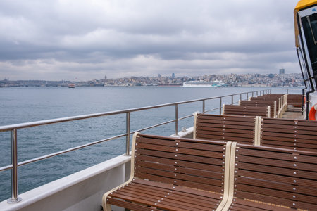 Wooden benches on the deck of a ferry boat with the city of Istanbul. Ferry boat sailing on the Bosphorus with the Istanbul skyline in the background. Cloudy dayの写真素材