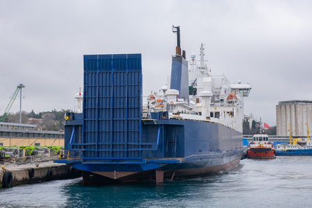 Large ferry boat docked at a port. White and blue ferry boat is moored at pier. Modern ship with...