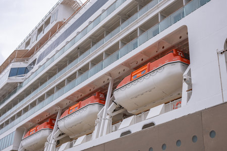 Large cruise ship with lifeboats docked at port, showing safety equipment and balcony cabins. Orange emergency passenger life boats on a white modern cruise linerの写真素材