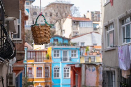 Colorful wicker basket hanging in narrow street in Balat district, Istanbul. Traditional Turkish wicker basket hanging in historic neighborhood with brightly painted colorful houses in backgroundの写真素材