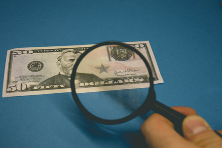 fifty dollar bill on a blue background being studied through a magnifying glassの写真素材