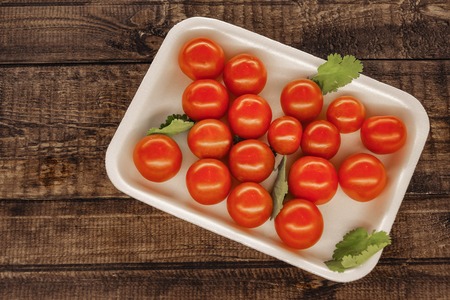 red cherry tomatoes on a white plate with a wooden background.の写真素材