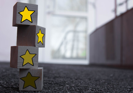 4 wooden cubes with a pattern of a yellow star standing on top of each other on asphalt.