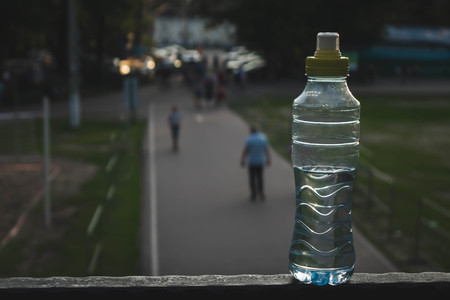 Plastic bottle top full with water with yellow cap in a park or garden with green trees in blurred...