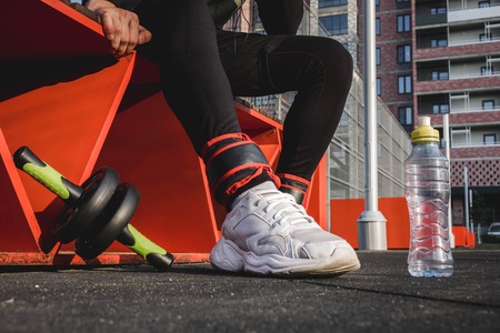 a man sits on an orange bench in black pants and white sneakers on the sports fieldの写真素材