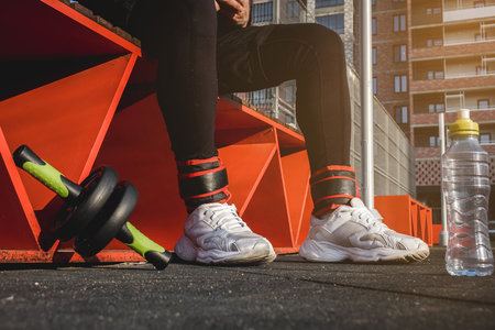 a man sits on an orange bench in black pants and white sneakers on the sports fieldの写真素材