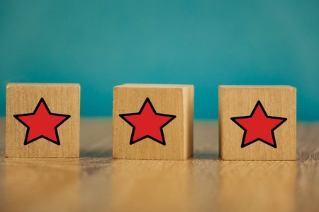 Red stars on wooden cubes on a blue background. Stars mean assessing quality. five-point rating systemの写真素材