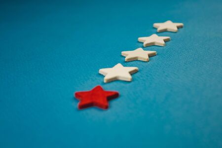 a bunch of wooden stars and one of them is highlighted in red. subject on blue background.