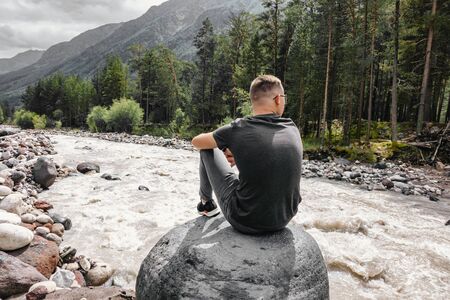 tourist sitting on a stone near a mountain river in the forest.の写真素材