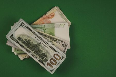 Dollars bundle, rubles and euros on green background. Cash stacks of different size. Earned with...
