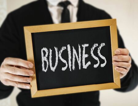 male businessman in a suit with tie holds in his hand a sign with the inscription BUSINESSの写真素材