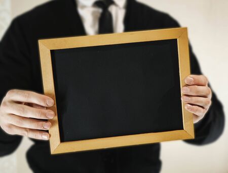 male businessman in a suit with tie holds in his hand a blank nameplateの写真素材