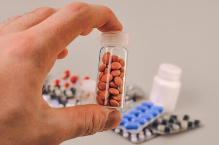 glass flask with orange pills in hand, which is full of drugs and pills