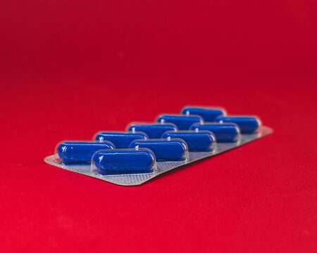 pack of blue capsule tablets on a red background.の写真素材
