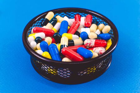 pile of pills of different colors in a black basket against a blue backgroundの写真素材