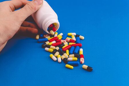 Man hand pours out multicolored pills on blue backgroundの写真素材