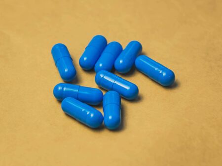heap of blue capsule tablets on a brown background.