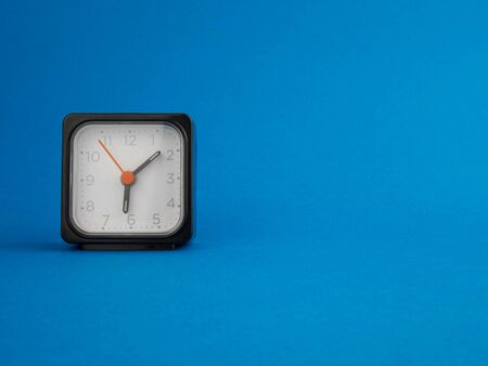 black table clock on the left, on a blue background.