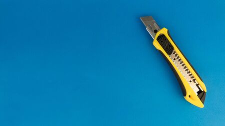 yellow office knife lying on a blue background.の写真素材