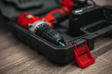 red electric drill lies in a dark suitcase on a wooden table.