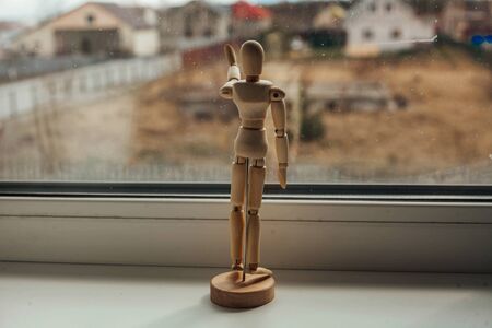 a wooden figurine looks out the window. concept of a man in quarantine.の写真素材