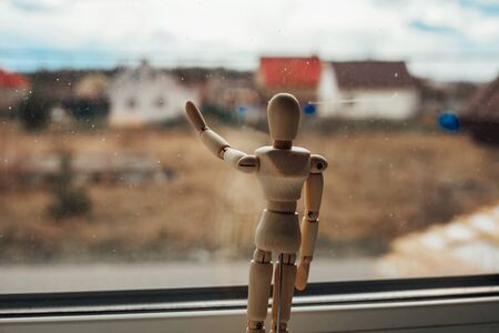 a wooden figurine looks out the window. concept of a man in quarantine.
