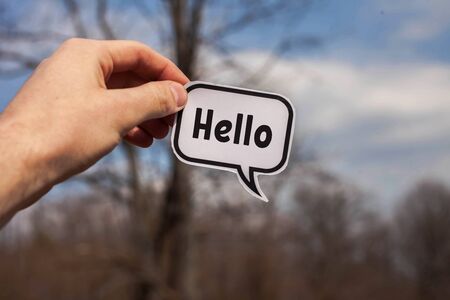a hand holds a paper cloud with the word hello on the background of treesの写真素材