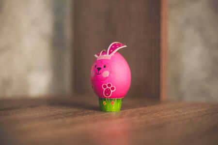 Easter egg in the form of a pink rabbit on a wooden table.の写真素材