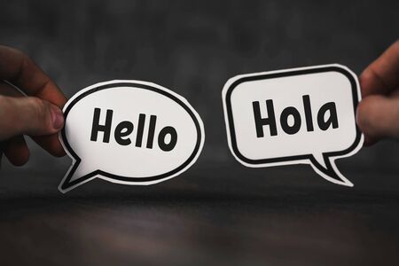 hands hold pieces of paper with the words hello and hola.の写真素材