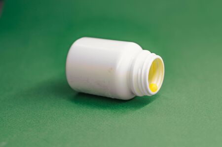 yellow vitamins in an open white packaging against a green background. Concept of medicineの写真素材