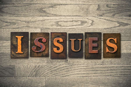 The word "ISSUES" theme written in vintage, ink stained, wooden letterpress type on a wood grained background.の写真素材