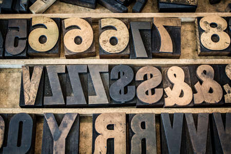 A vintage drawer of old wooden letterpress letters, numbers, and symbols. Type is ink stained and photographed with the letters naturally backwards as they normally appear before printing.の写真素材