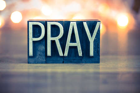 The word PRAY written in vintage metal letterpress type on a soft backlit background.