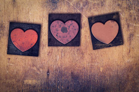 Three dirty inked stained vintage letterpress hearts on a aged wooden background.の写真素材