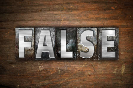 The word "False" written in vintage metal letterpress type on an aged wooden background.の写真素材
