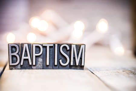 The word BAPTISM written in vintage metal letterpress type on a bokeh light and wooden background.の写真素材