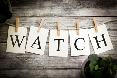 A set of printed cards spelling the word WATCH on an aged wooden background.の写真素材