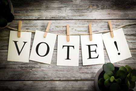 A set of printed cards spelling the word VOTE on an aged wooden background.の写真素材