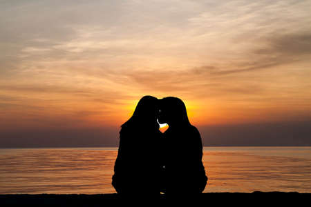 Silhouette of female homosexuals in love beside seaの写真素材