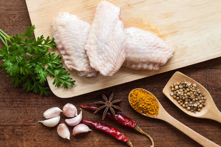 raw chicken wings on chopping board with spicesの写真素材