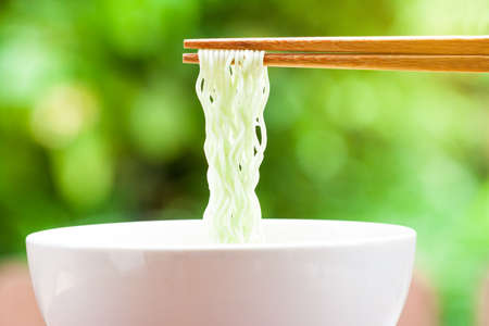 green instant noodles in chopsticks on green backgroundの写真素材