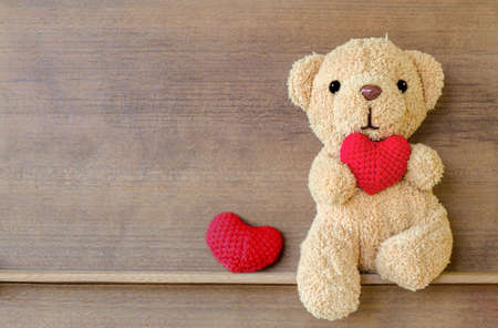 Teddy bear holding a heart-shaped pillow on wood shelf board backgroundの写真素材