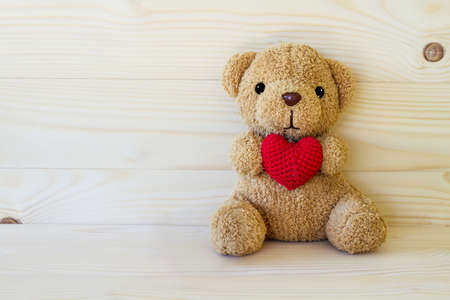 Teddy bear holding a heart-shaped pillow on wood board backgroundの写真素材