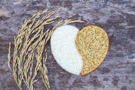 paddy rice and white rice in heart-shaped plastic box on old wood backgroundの写真素材
