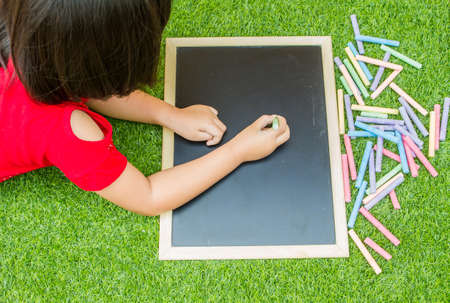 Little asian girl writing blackboard on green grassの写真素材