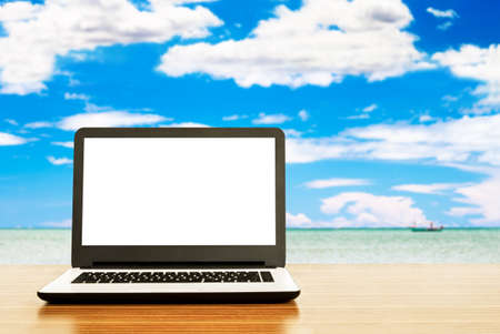 Laptop with blank screen on table, beautiful sea background, travel conceptの写真素材