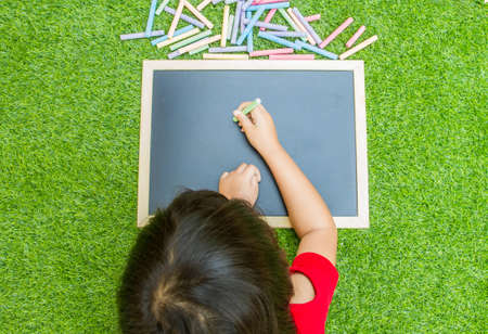 Little asian girl writing blackboard on green grassの写真素材