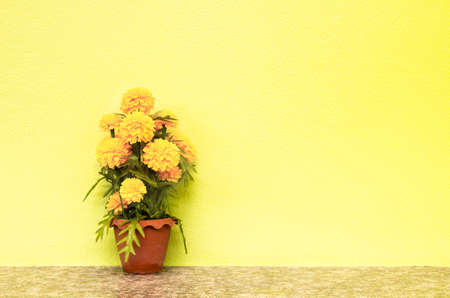 artificial marigold flower in plastic vase on yellow concrete wall backgroundの写真素材