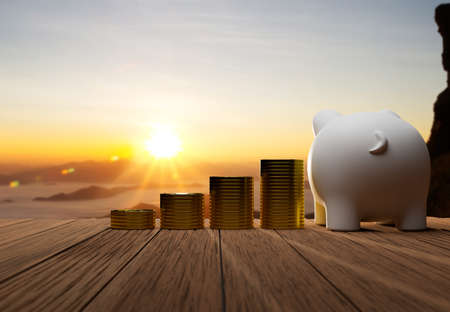 Piggy bank and a pile of coins on old wooden desk with beautiful sunrise background, Saving money...