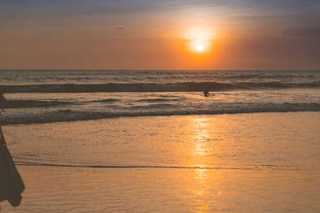 People bathing in the sun in sunset, swiming and playing games on the beach. Tourists on the sand beach in Bali, Indonesiaの写真素材